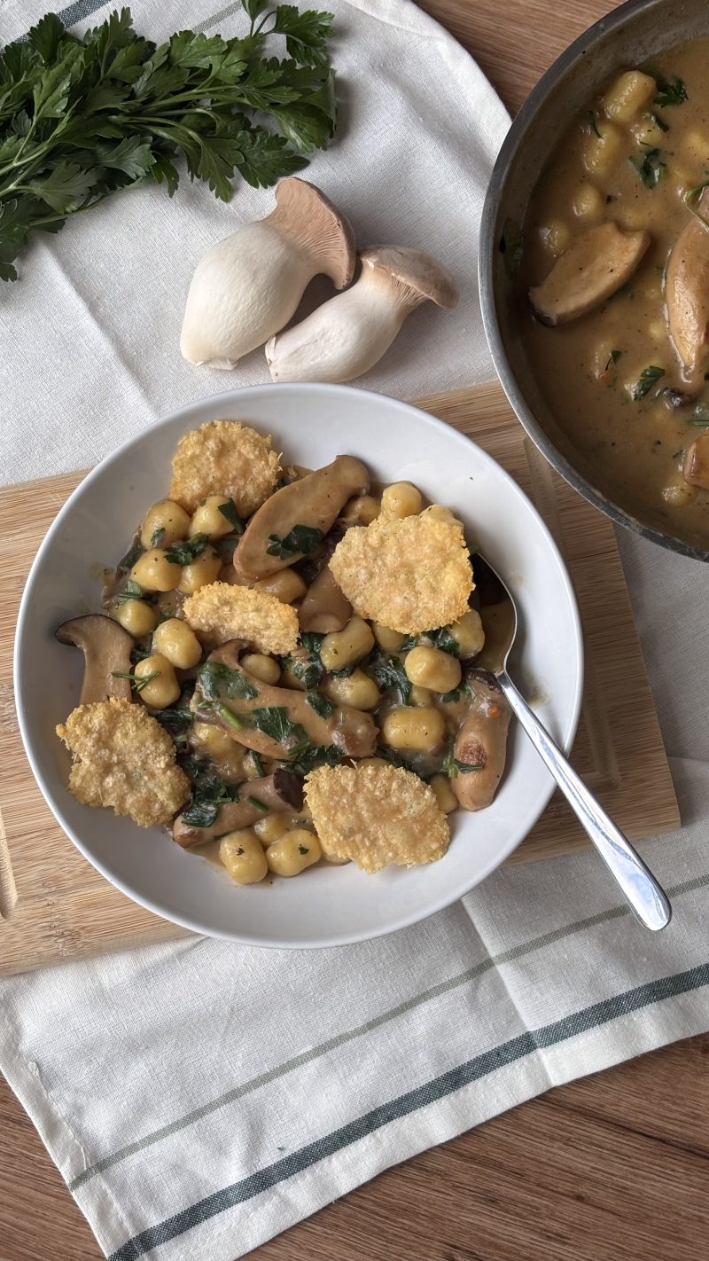 Ein Teller Gnocchi in cremiger Kräuterseitling-Pilzrahmsauce, garniert mit Petersilie und Parmesanchips.