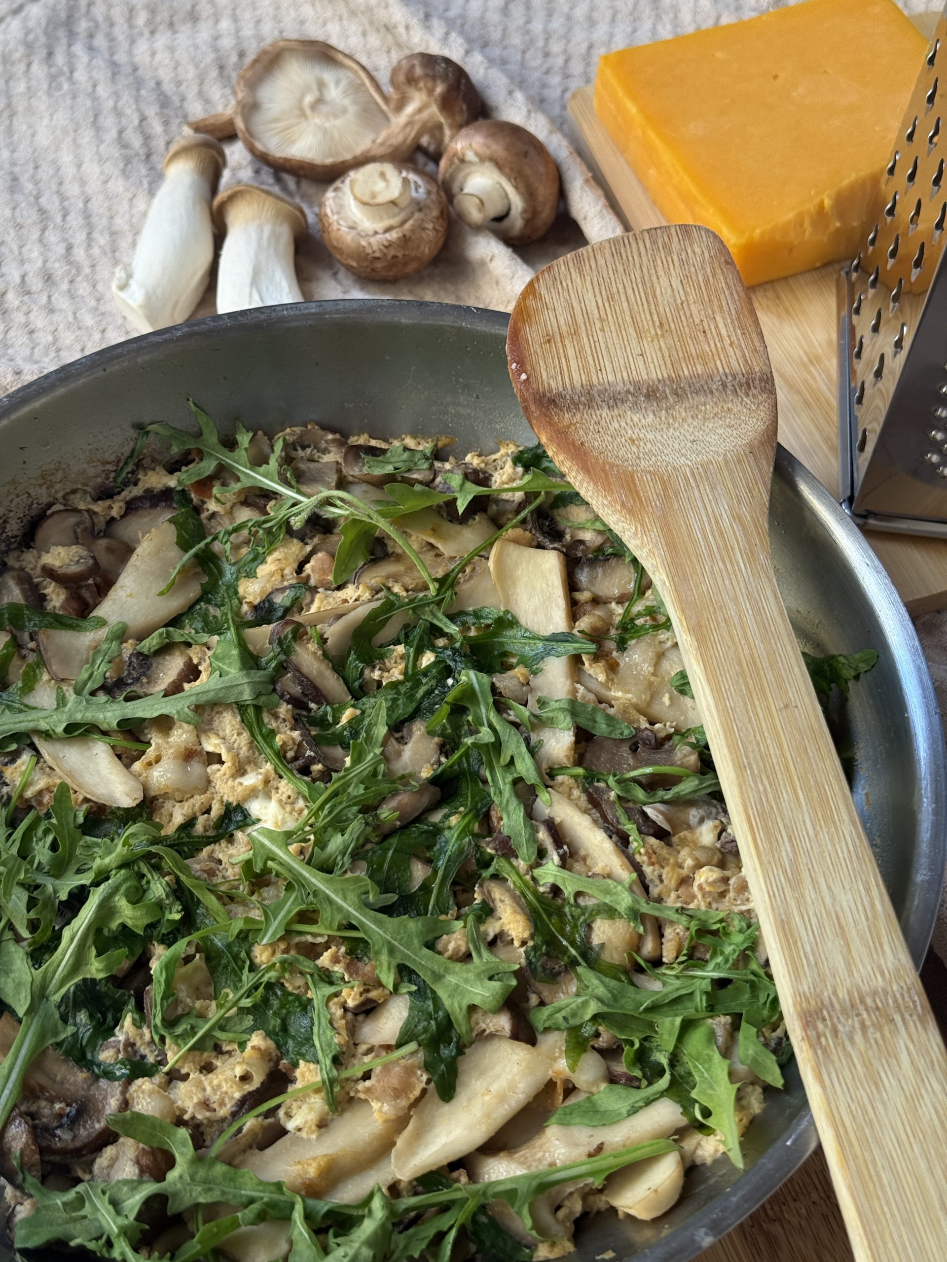 Frittata mit gemischten Pilzen, Räucherspeck, Cheddar und Rucola auf einem Holzbrett.