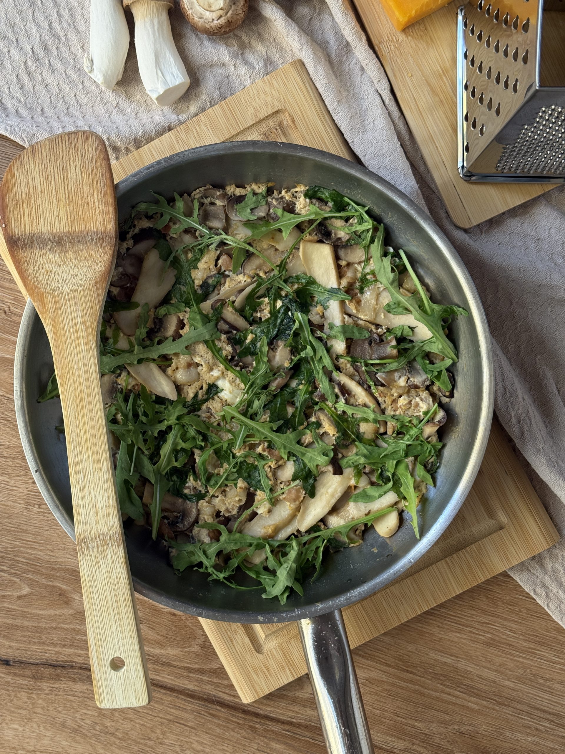 Frittata mit gemischten Pilzen, Räucherspeck, Cheddar und Rucola auf einem Holzbrett.