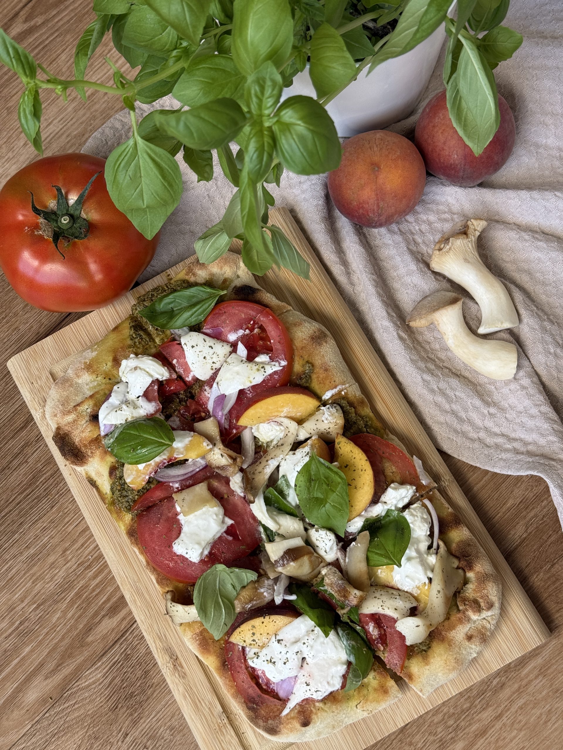 Sommerliche Pinsa mit Pfirsich, Tomate, Burrata, Kräuterseitlingen, roter Zwiebel und Basilikum.