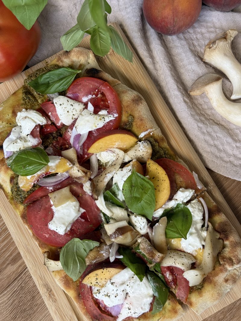 Sommerliche Pinsa mit Pfirsich, Tomate, Burrata, Kräuterseitlingen, roter Zwiebel und Basilikum.