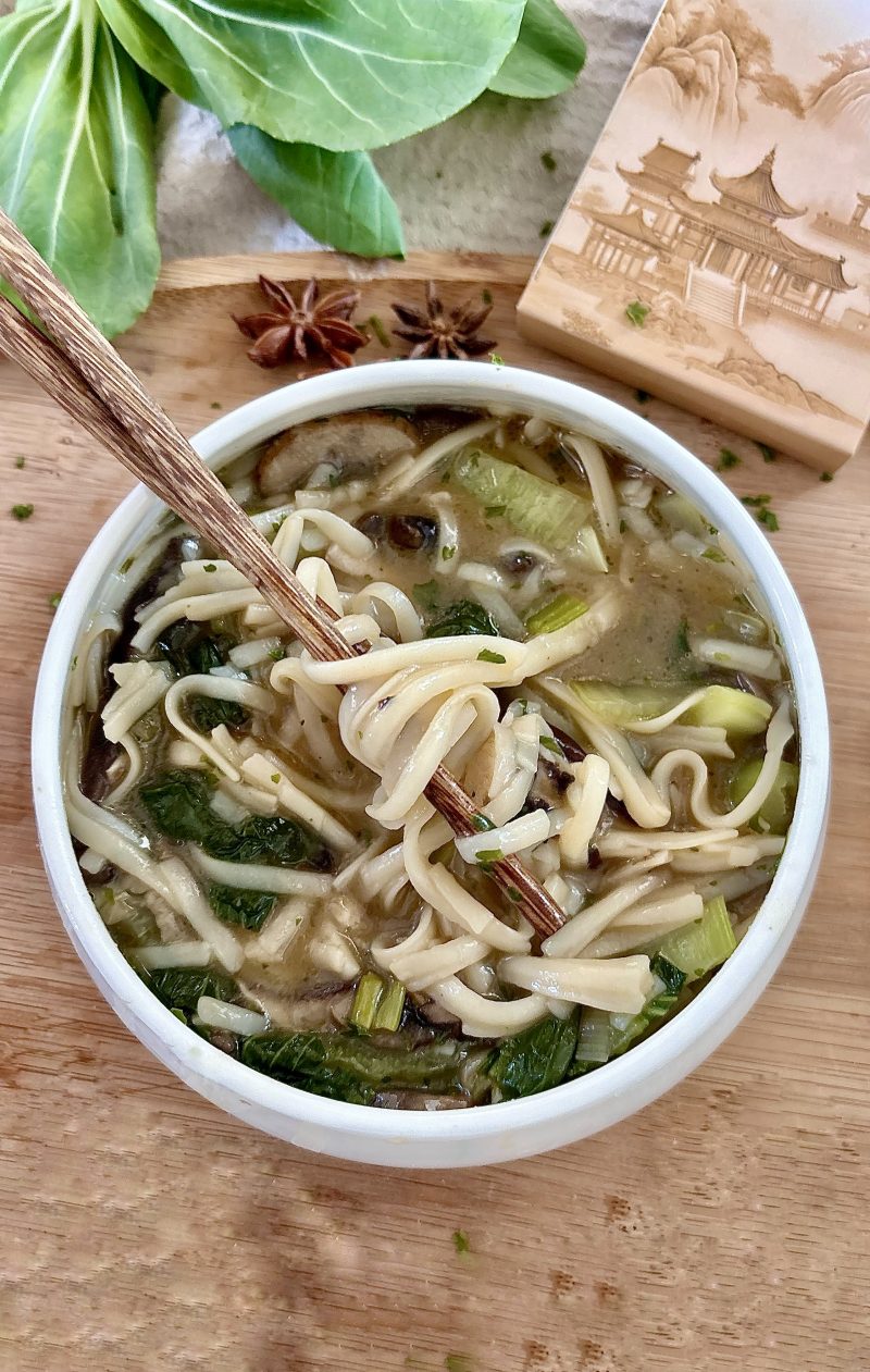 Pho-Suppe mit Shiitake, Champignons, Reisnudeln, Pak Choi und frischen Kräutern in einer Schüssel serviert.