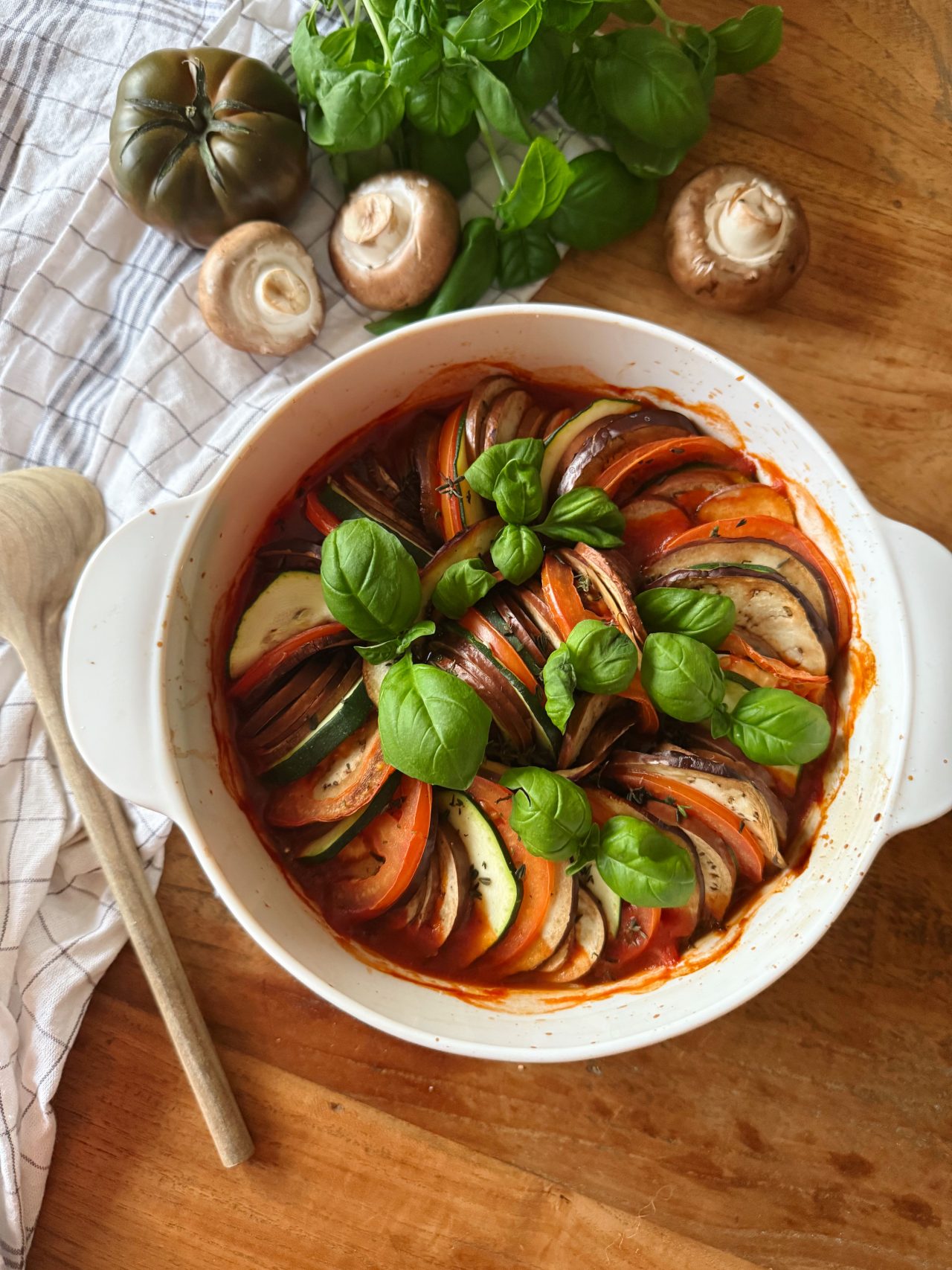 Ofen-Ratatouille mit Champignons, Zucchini, Auberginen und Tomaten, geschichtet und mit Kräutern garniert.